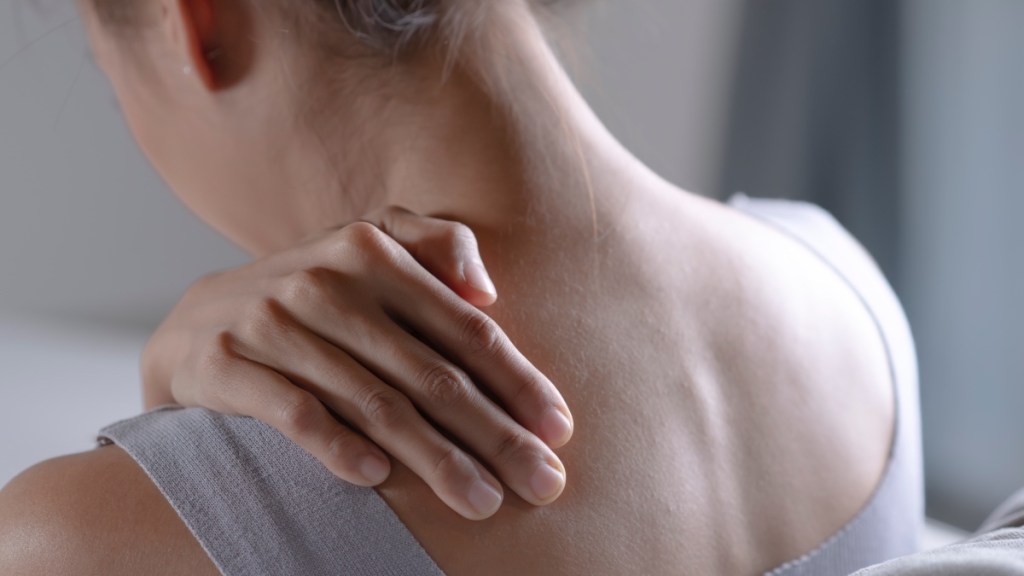 A close-up of a woman touching the back of her shoulder in pain