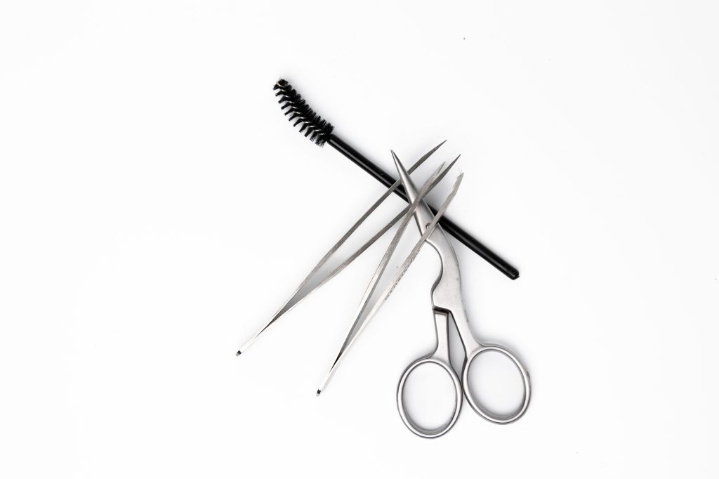 Scissors, tweezers and a spoolie brush, all tools that are used for how to tweeze eyebrows