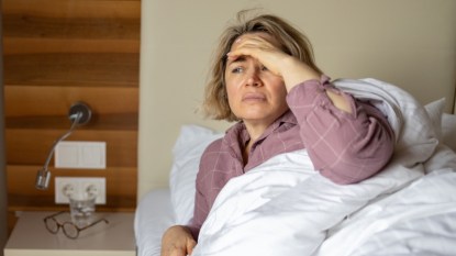A woman in purple pajamas lying in bed with her hand on her head because she's waking up dizzy