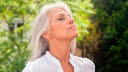 A woman with grey hair and closed eyes who is breathing deeply thanks to COPD self-care