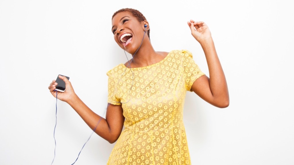 An African American woman wearing a yellow dress holding an MP3 player while singing along to enjoy the benefits of neural nostalgia