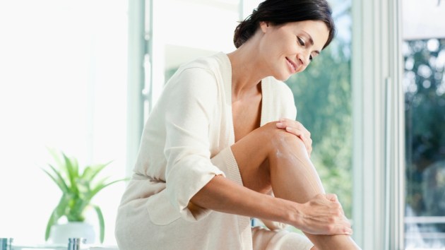 mature woman putting body lotion on legs