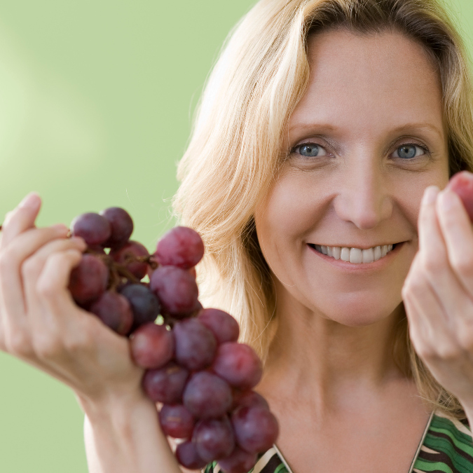 woman happily holds a cluster of red grapes