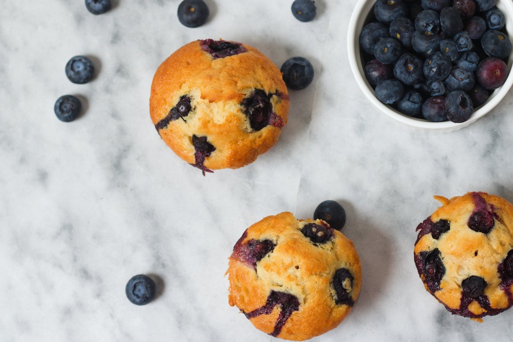 Top view of muffins with blueberries next to bowl of blueberries