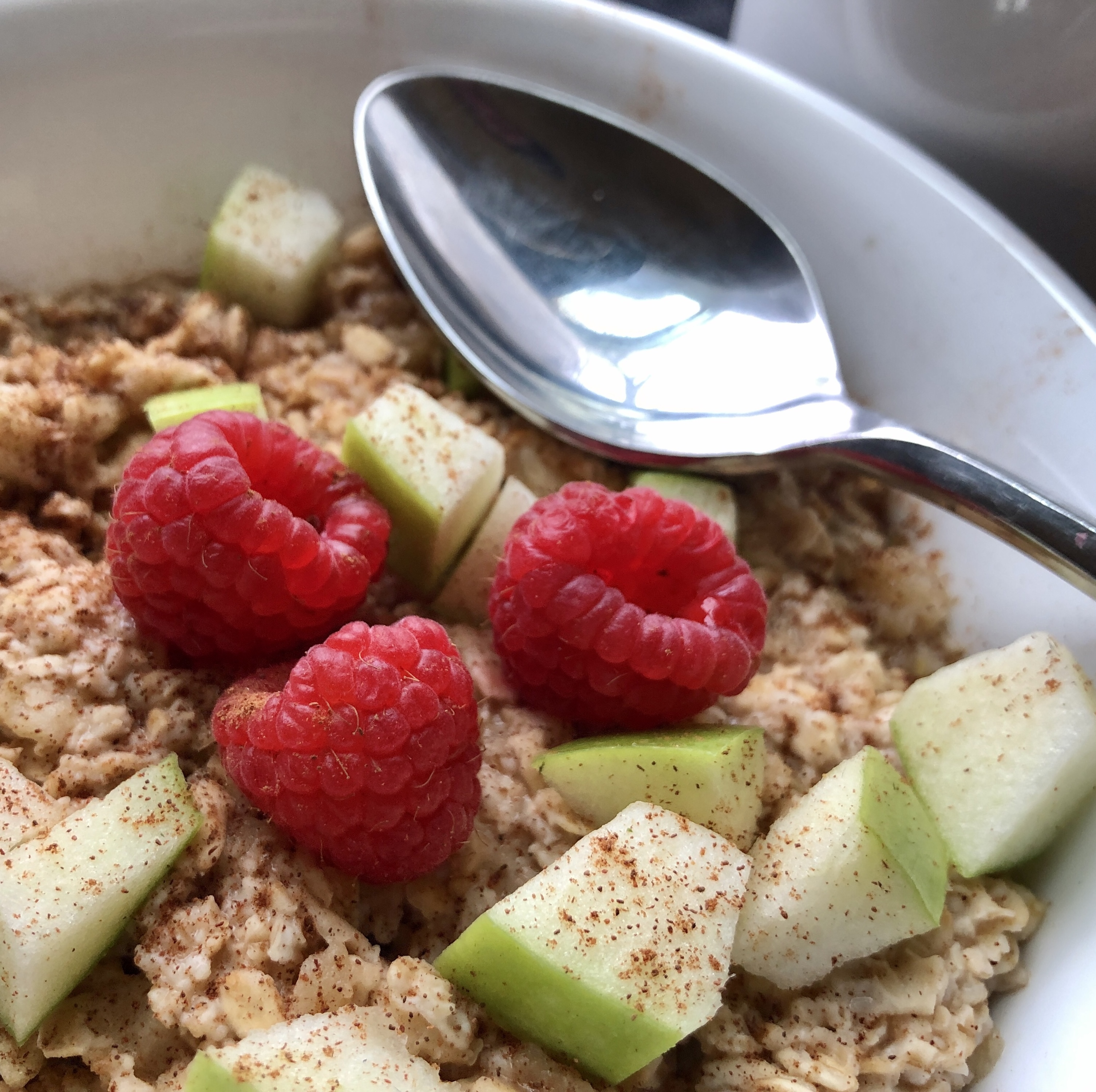 closeup of apple, cinnamon, raspberry oatmeal with spoon
