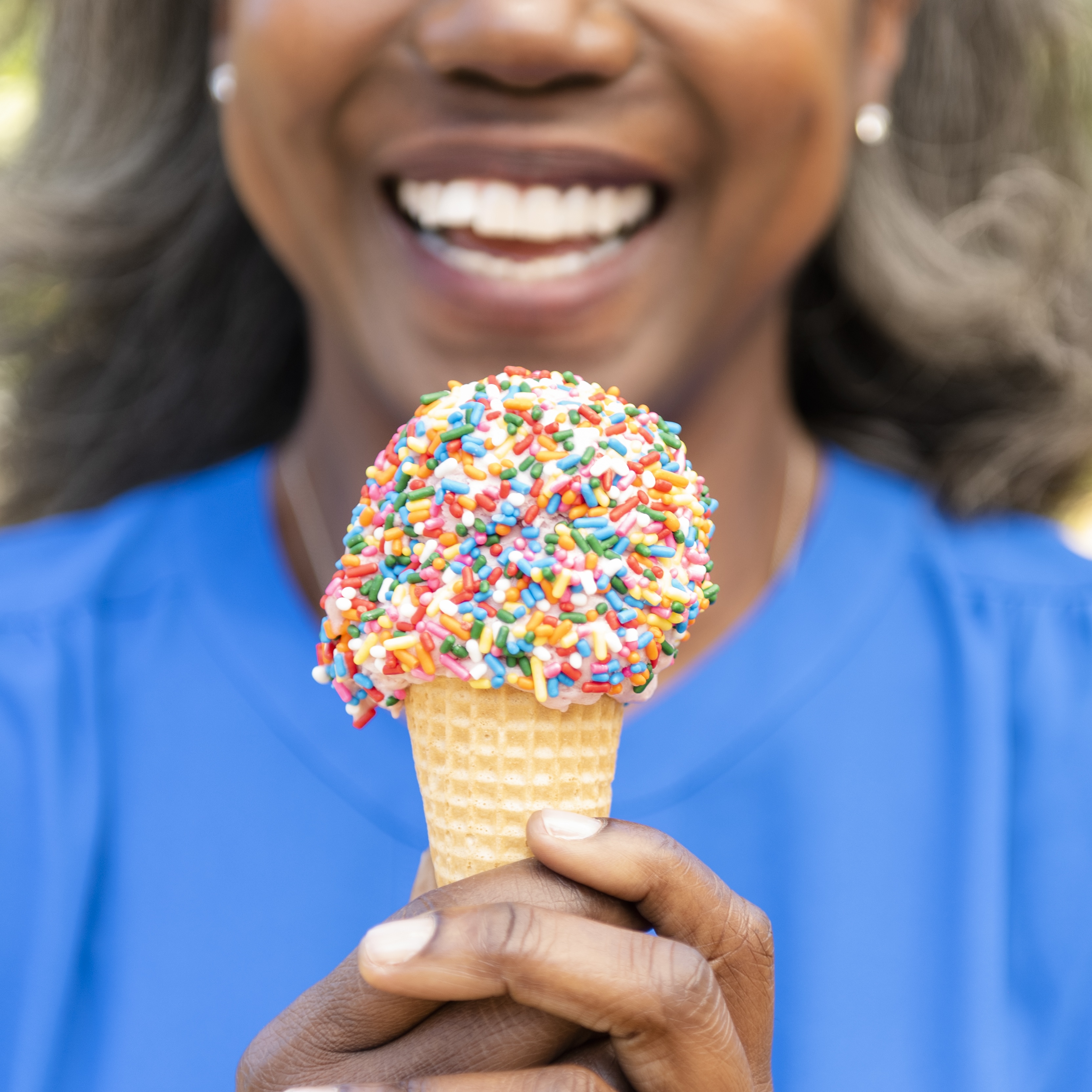 closeup of woman smiling eating ice cream cone with rainbow sprinkles during diet cheat day