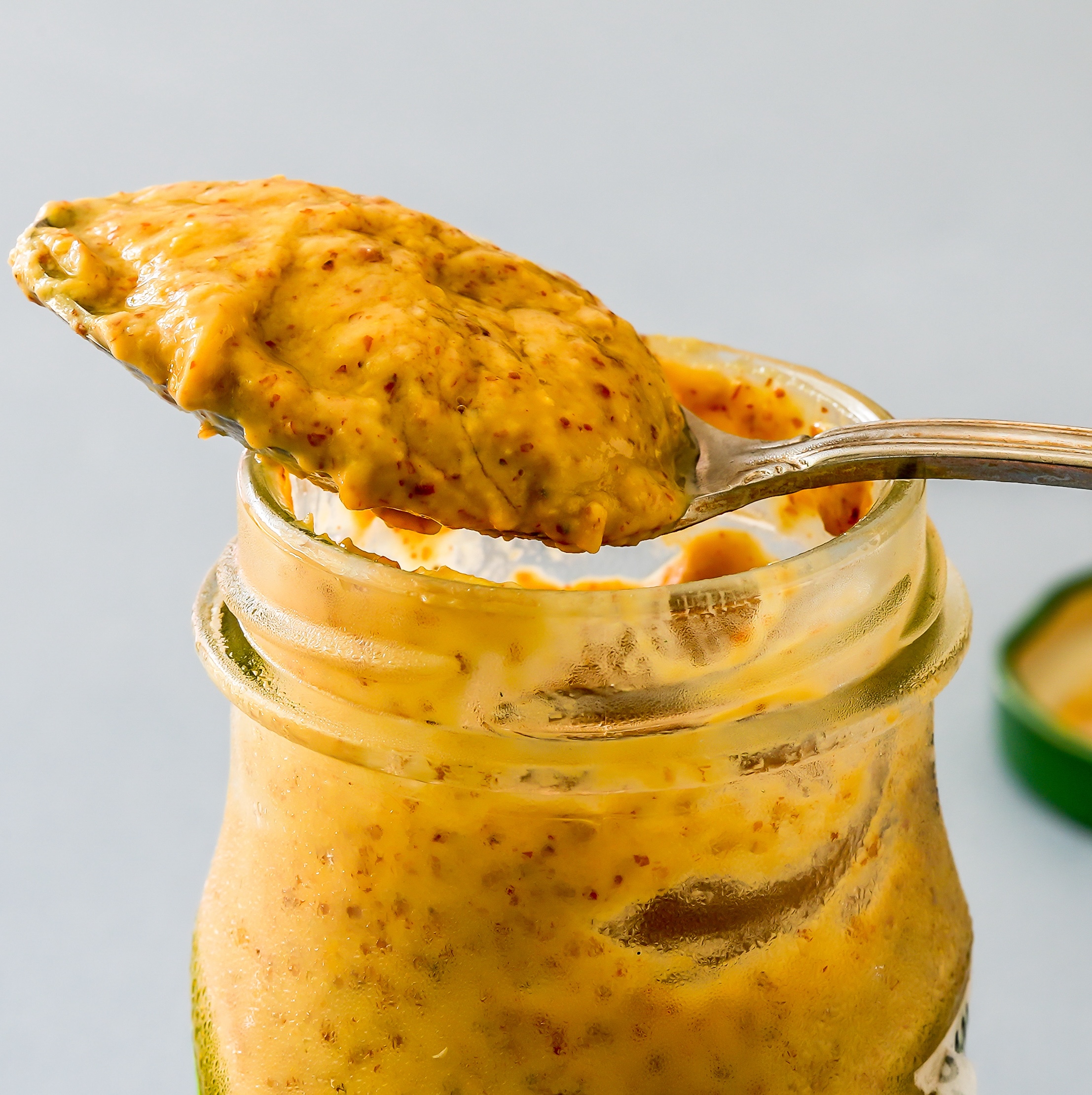 Spoonful of mustard resting on top of mustard jar