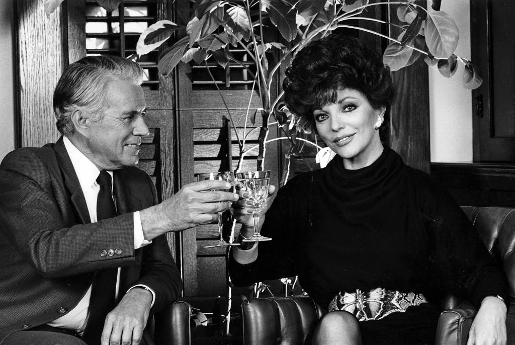 Joan Collins and John Forsythe share a toast in the boardroom of Producer Aaron Spelling during the 1985 season of the TV series Dynasty