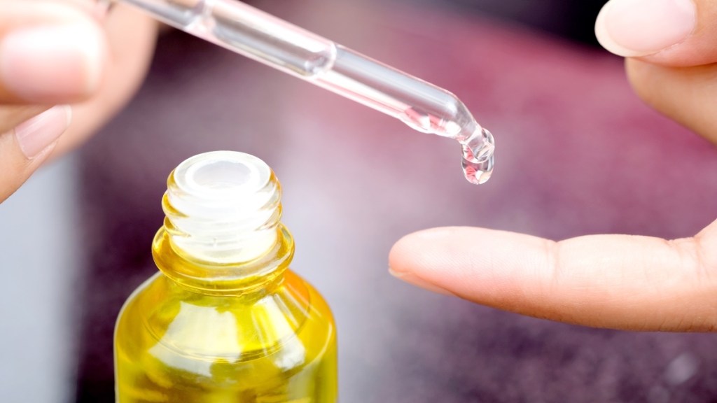 Close-up of a woman applying a dropper of vitamin E oil to her finger