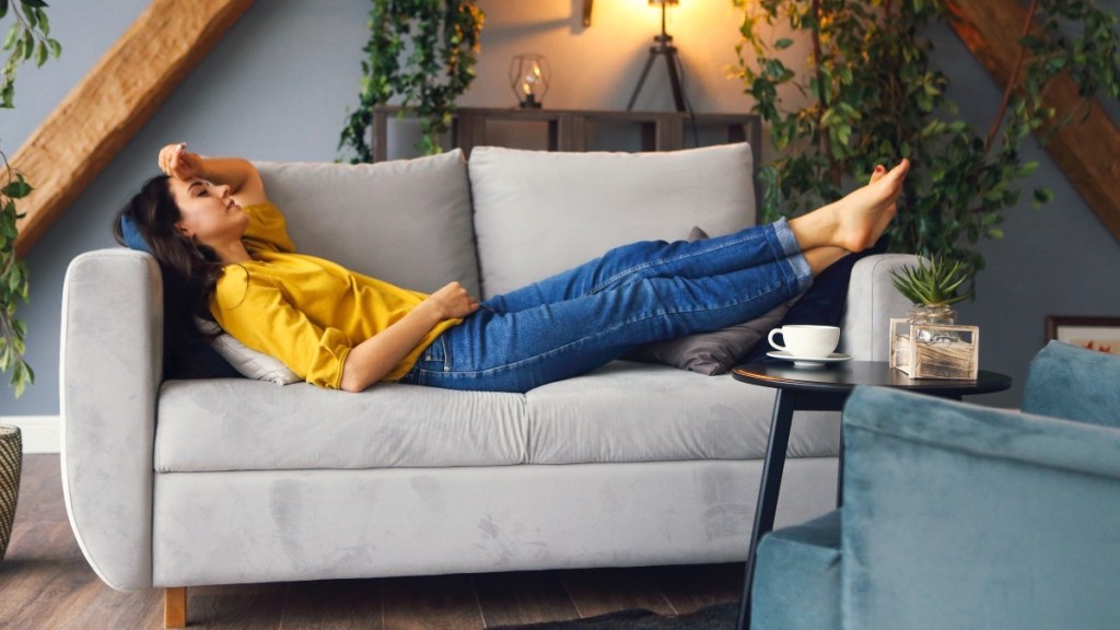 A brunette woman in a yellow shirt and jeans lying on a couch with her legs up to treat a skin ulcer