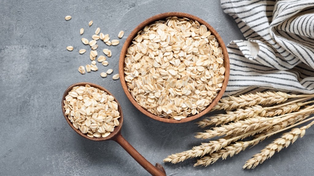 A bowl of rolled oats on table beside fresh wheat