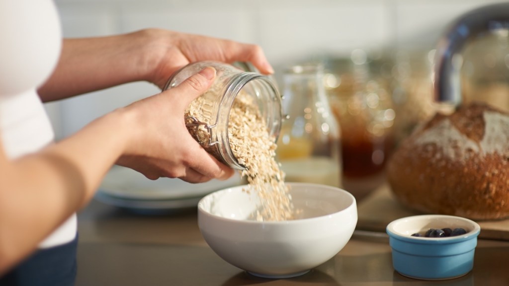 A close-up of a woman pouring oats into a while bowl as part of the oatzempic diet 