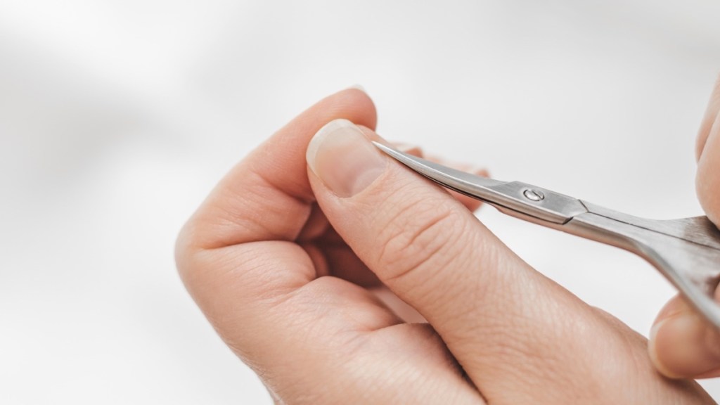 A close-up of a woman using cuticle scissors to trim a hangnail on her thumb