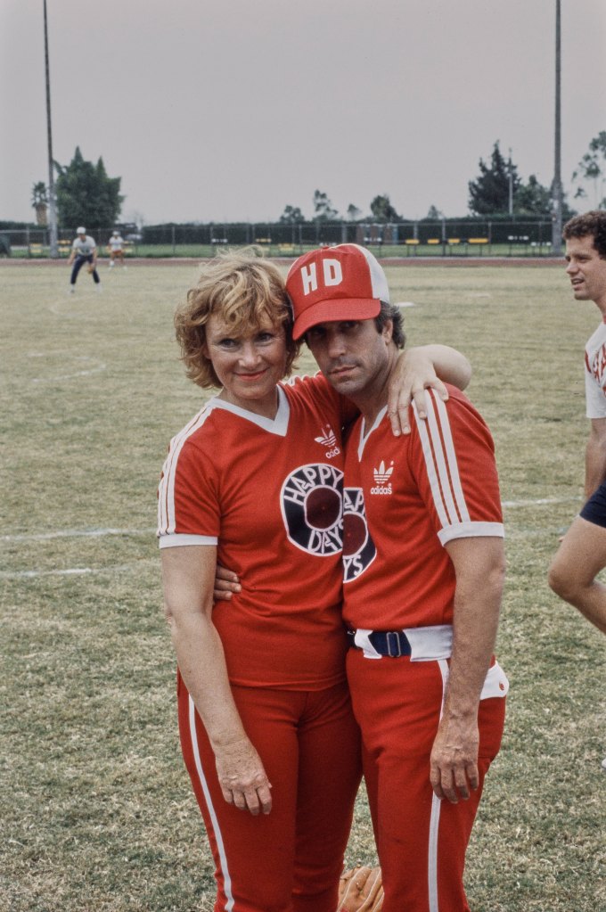 Marion Ross with her arm around the shoulders of American actor Henry Winkler, both wearing red Adidas sportswear with white trim and 'Happy Days' prints on the chest, with Winkler also wearing a 'HD' baseball cap, circa 1980.