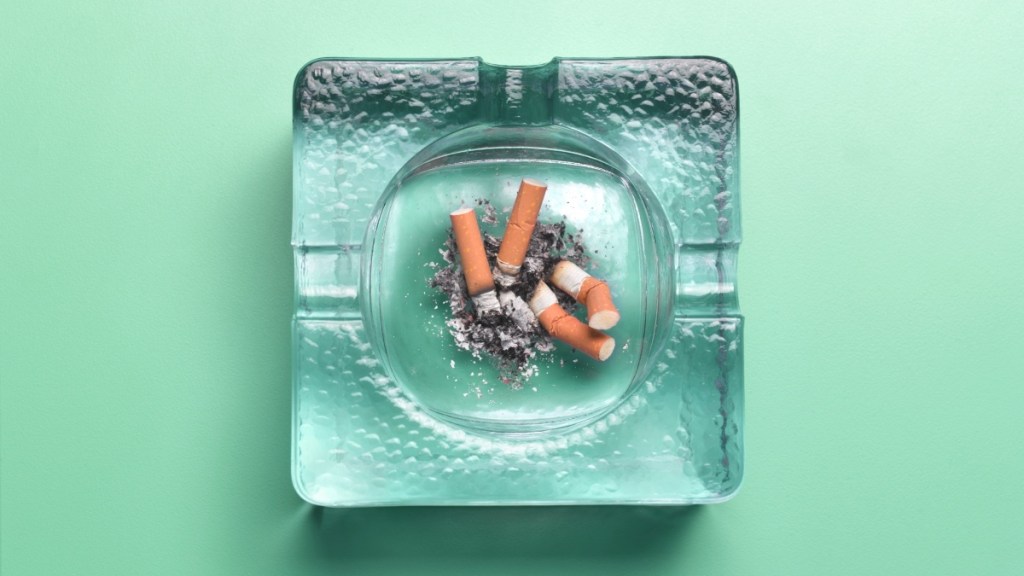An ashtray with cigarettes against a green background