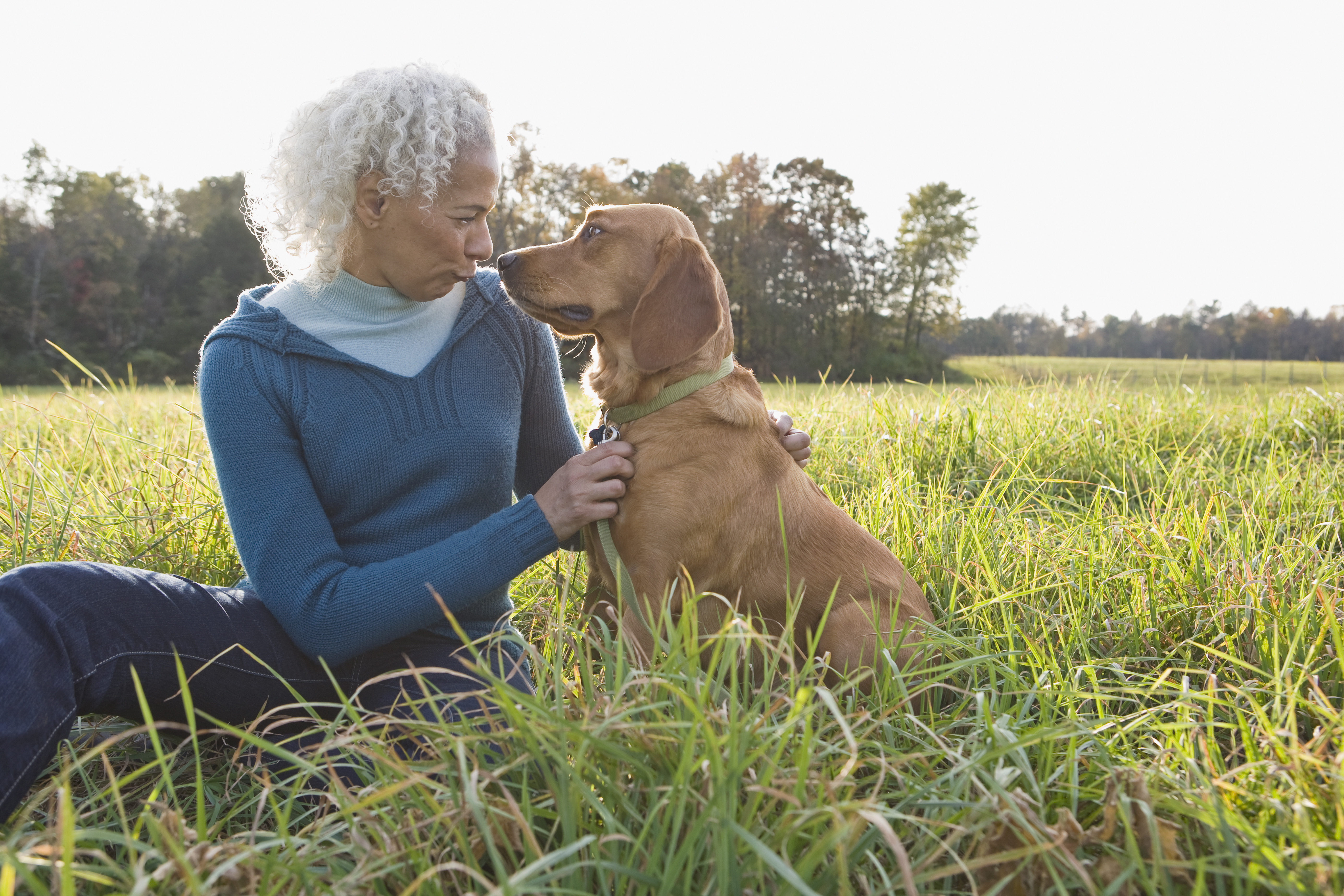 Woman and her dog sitting in the grass looking at one another