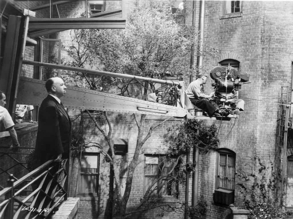 Alfred Hitchcock observes the action from a balcony as cameramen extended out on an "arm" film a scene on the set of "Rear Window"