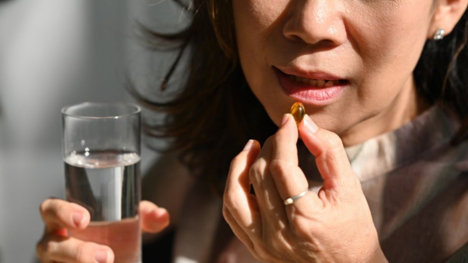 Close up shot of woman's hand taking fish oil or omega-3 supplement capsule as part of arthritis pain relief