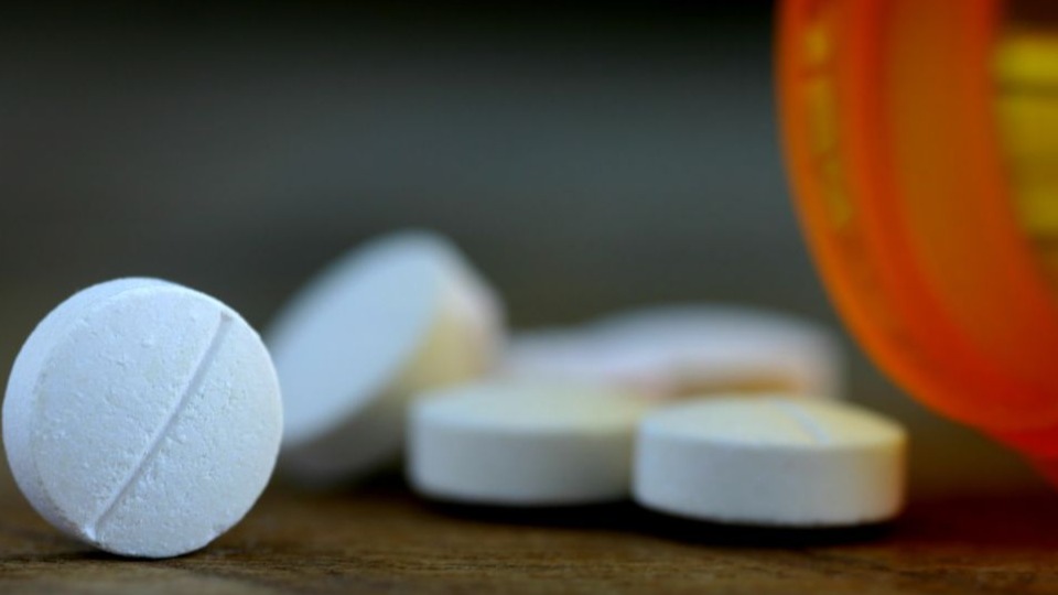 closeup of aspirin coming out of pill bottle on wooden surface