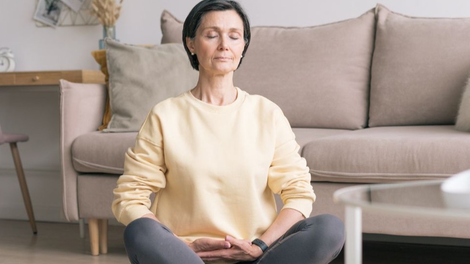 woman in lotus position meditating for blood sugar control with closed eyes at home while sitting on yoga mat on floor
