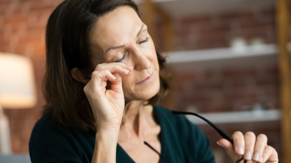 woman with eyes closed taking off her glasses and touching her eye