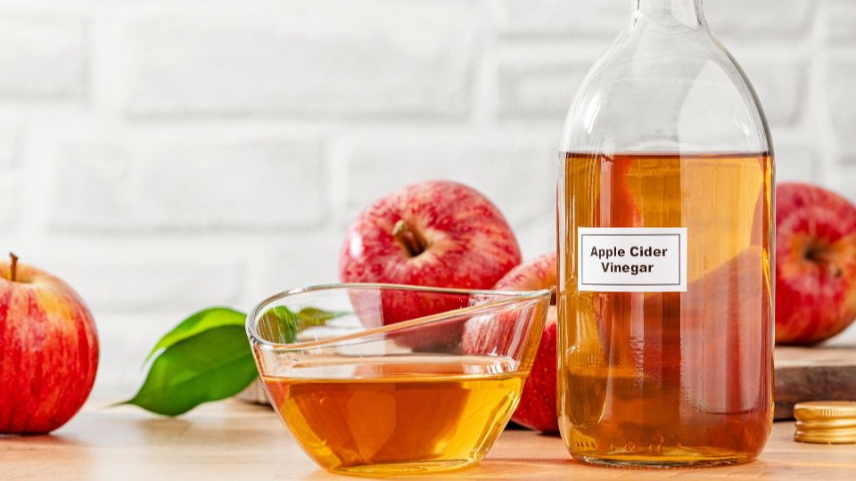Apple cider vinegar bottle and apple fruits on kitchen table