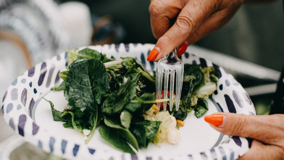 closeup of woman using plastic fork to eat salad off paper plate