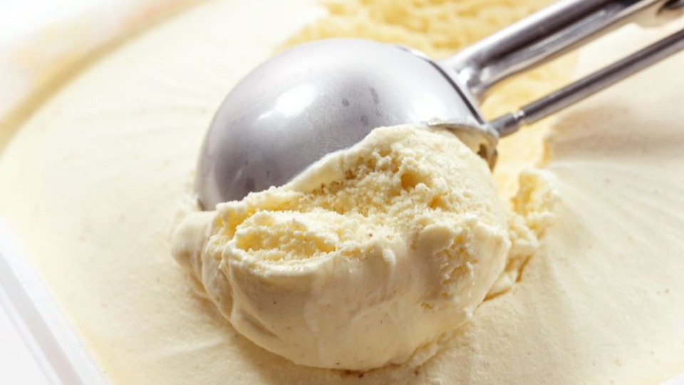 Metal scoop scrapes vanilla ice cream from the box