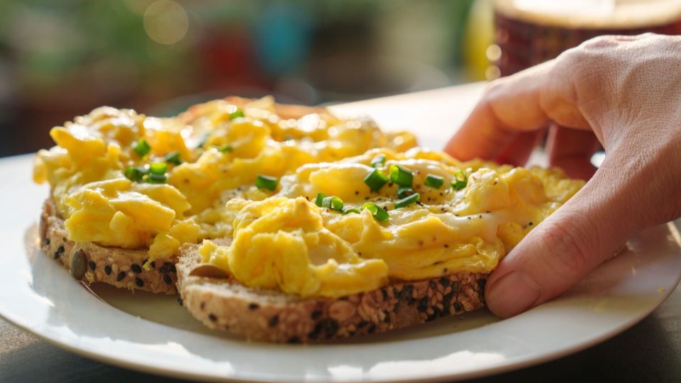 closeup of woman holding a piece of whole grain toast with eggs as part of a low carb diet for diabetics