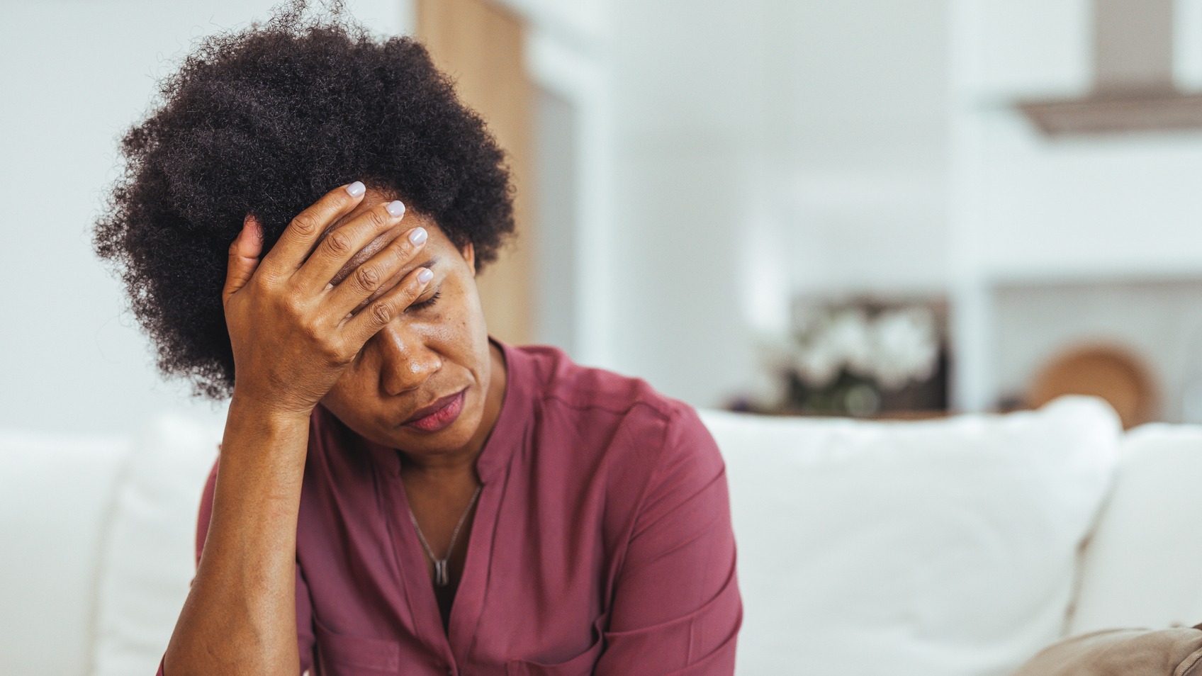 mature woman suffering from thyroid fatigue sitting on the couch with hand to forehead