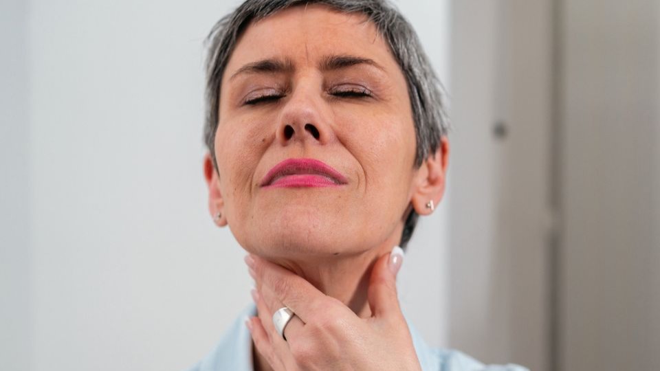 Woman touching front of her neck wondering what does thyroid pain feel like