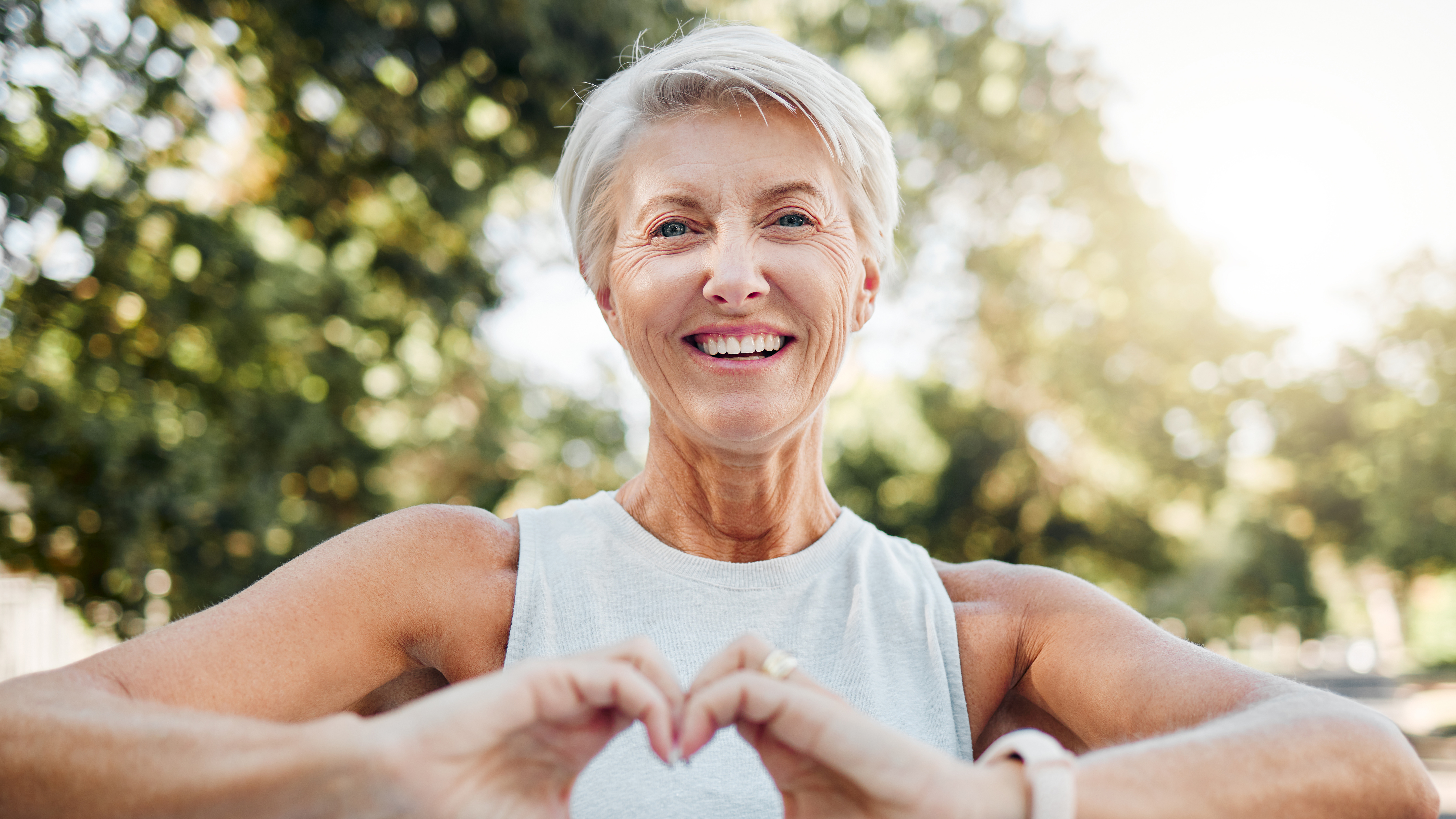 older woman happily out for a walk makes a heart with her hands over her own heart