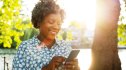 A mature Black woman smiling while holding her smartphone outdoors as she participates in the Scooby-Doo Virtual Challenge