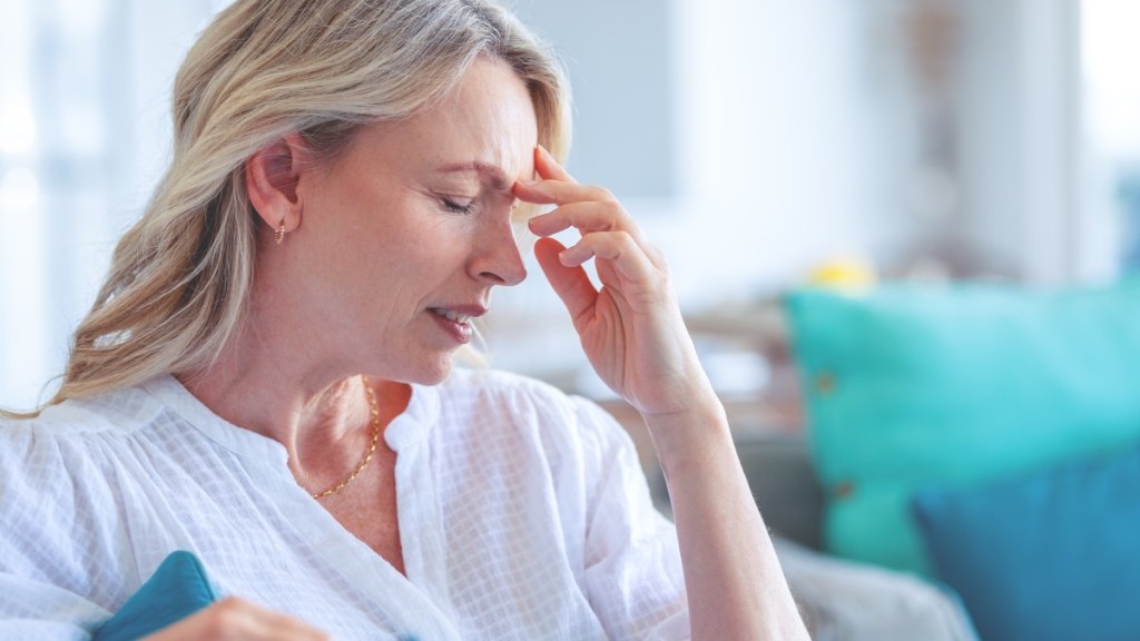 Mature woman in a white top with her hand to her head experiencing brain freeze