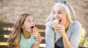 A mature woman sitting next to her granddaughter on a bench while eating ice cream and wondering what causes brain freeze