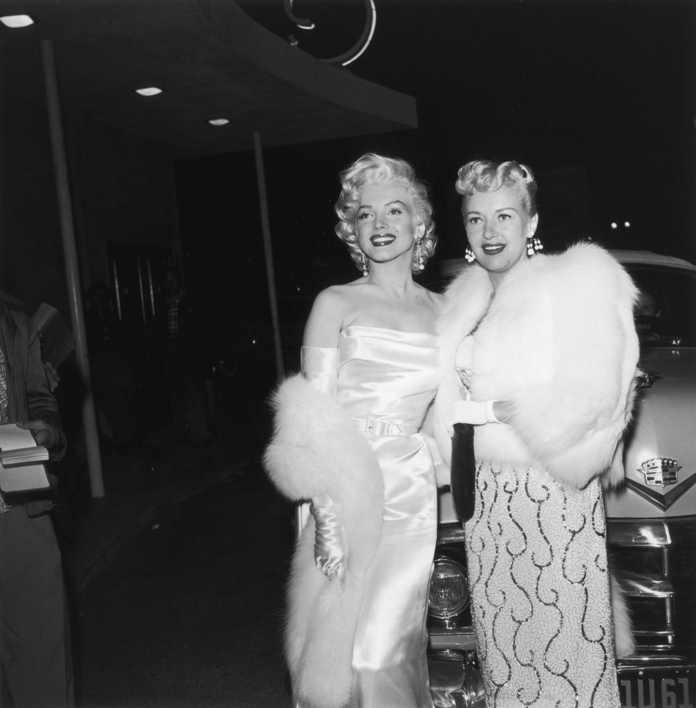 American actors Marilyn Monroe (1926 - 1962, left) and Betty Grable (1916 - 1973) at the premiere of director Jean Negulesco's film, 'How to Marry a Millionaire'. Monroe is wearing a strapless silk gown with matching long gloves with a fur wrap. Grable is wearing a beaded dress and a fur jacket