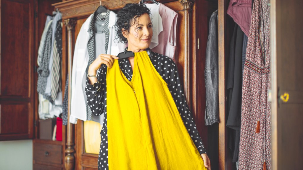 woman surveys her clothes in her closet, deciding what she wants to keep and what to toss, as she conquers clutter