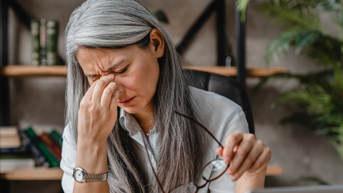 A mature woman holding her glasses and pinching the bridge of her nose while closing her eyes due to blurry vision, a symptom of high blood sugar