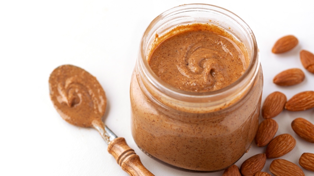 A jar of high-protein nut butter next to almonds and a spoon