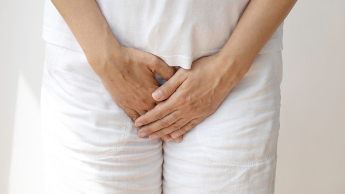 Close up of a woman wearing white clothes while holding her hands over herself due to pain from a recurrent yeast infection during menopause