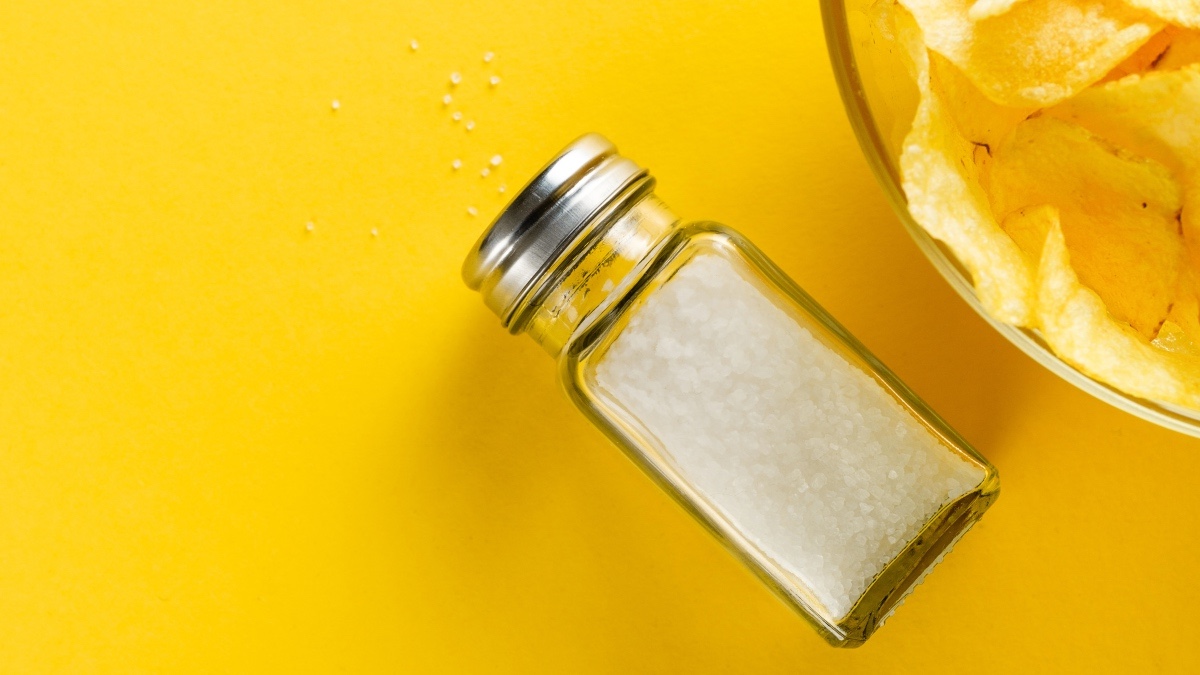 A salt shaker and bowl of chips against a yellow background