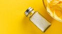 A salt shaker and bowl of chips against a yellow background