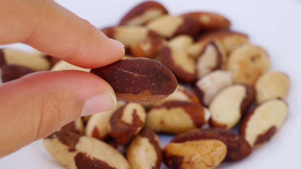 Close-up of a woman's hand holding Brazil nuts, which can help serve as a home treatment for thyroid eye disease