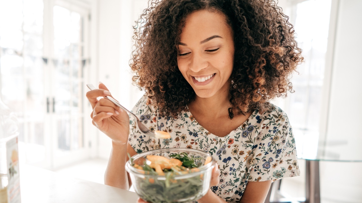 A woman eating a salad made with leafy greens, foods that can lower your blood sugar