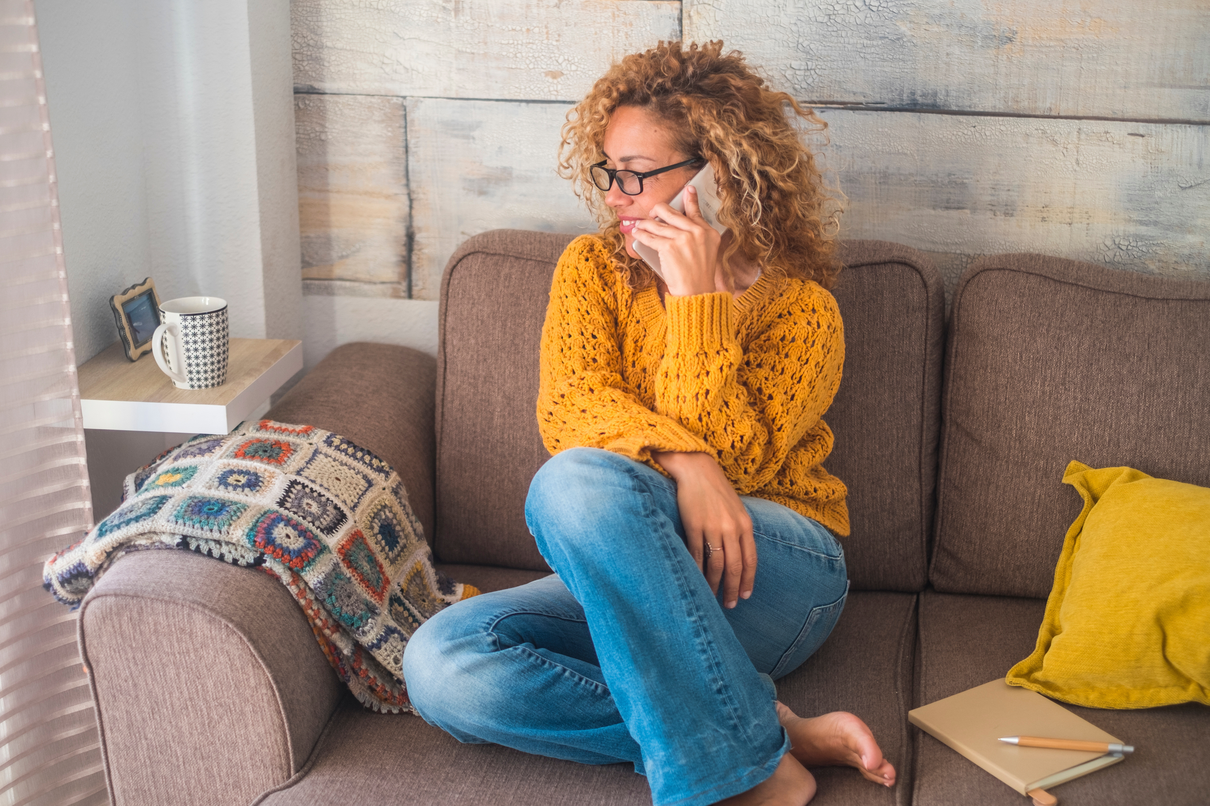A woman sits on her couch on the phone.