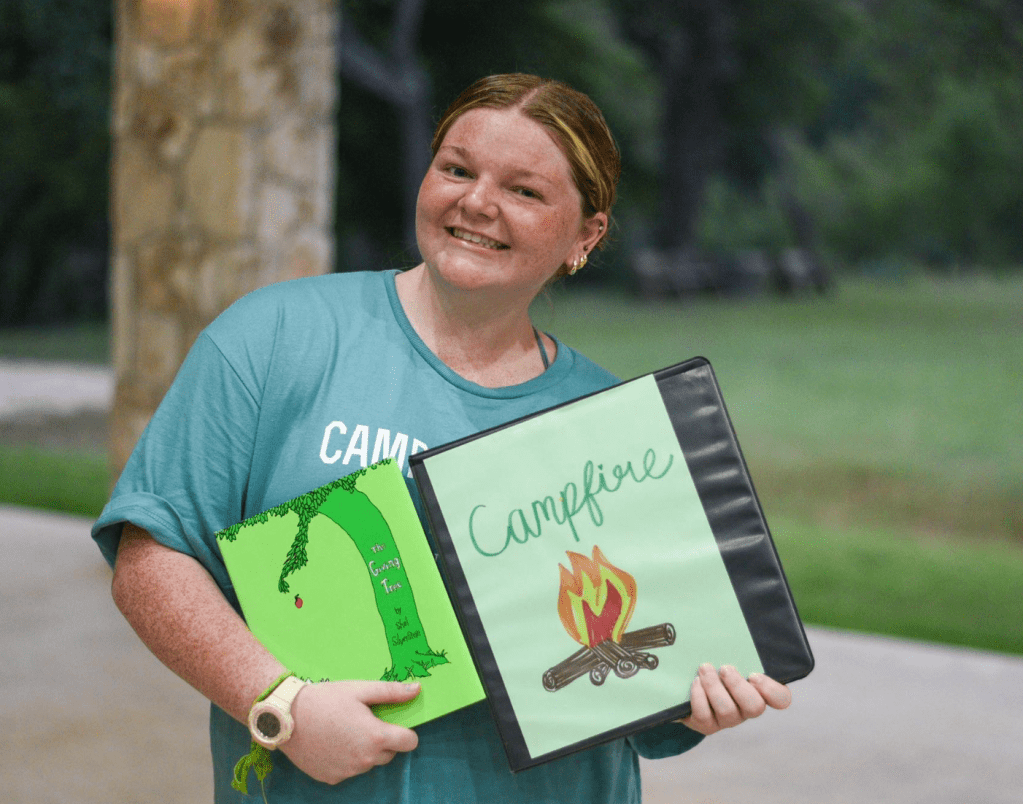 Emma Foltz smiling for a photo holding her camp binder. 