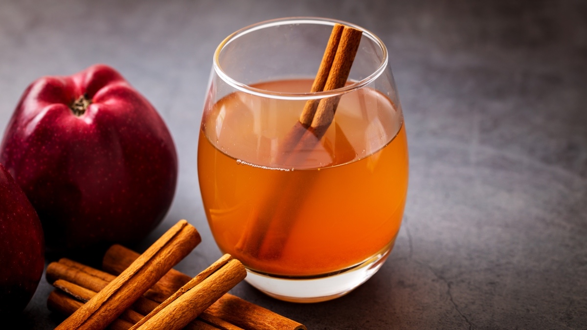 A glass of cinnamon water with fresh cinnamon sticks and an apple