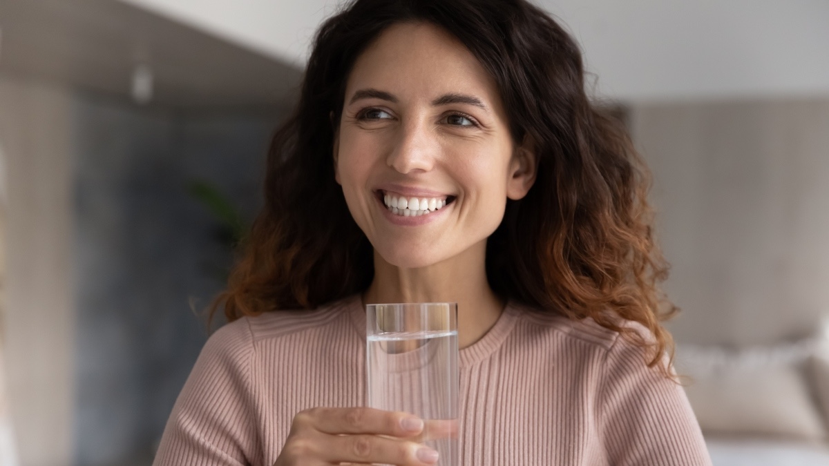 A smiling woman drinking a glass of water to lower her blood sugar
