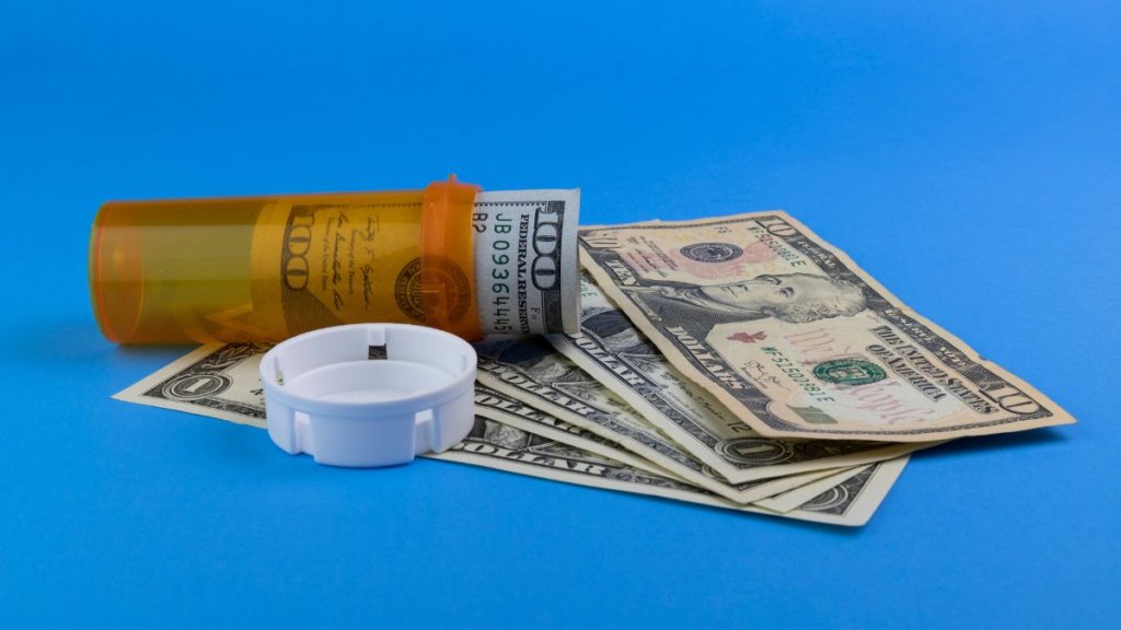 Hundred dollar bill and smaller dollar bills with a pill bottle representing the high cost of drug and opiate addiction.
