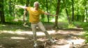An older woman smiling and balancing on one leg outdoors